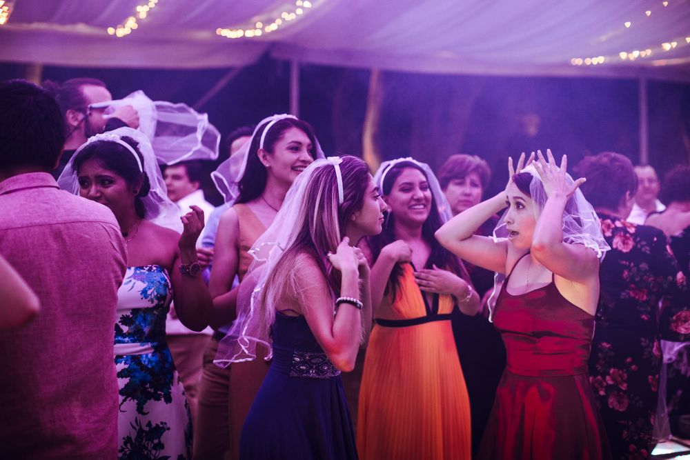 Wedding reception crowd dancing under purple ambient lighting in a decorated venue.