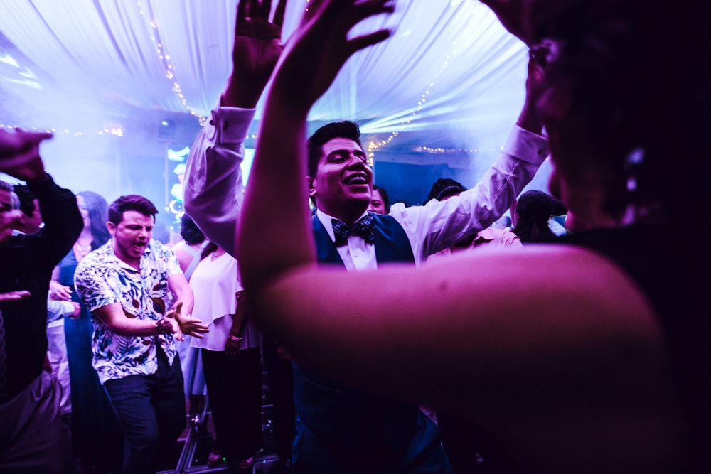 Wedding guests dance and celebrate on a colorful illuminated dance floor during an evening reception.