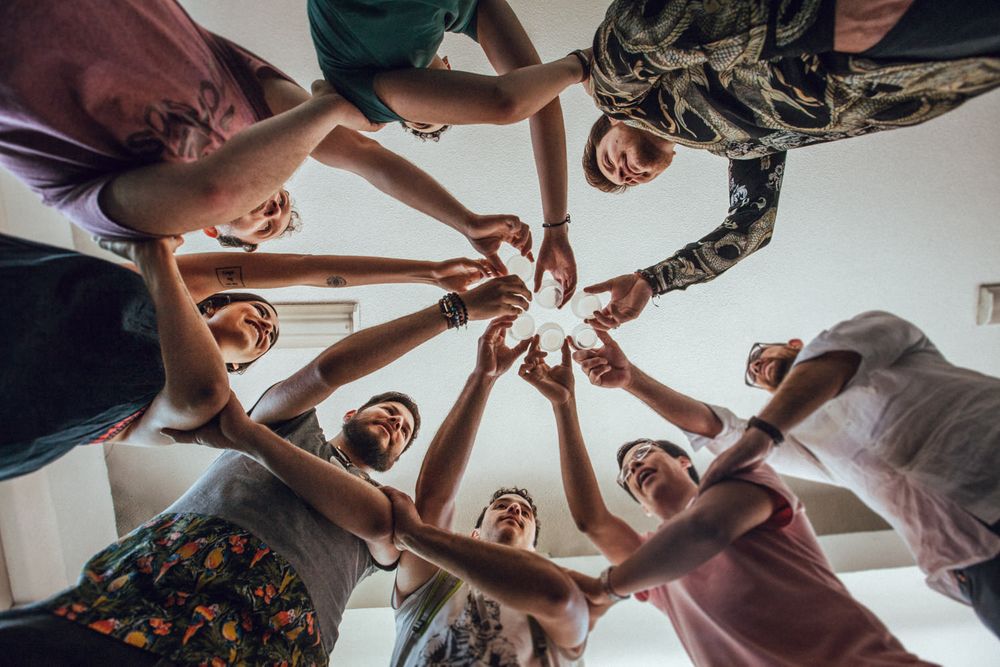 Group forming a circle with their hands joined together in unity from below perspective.