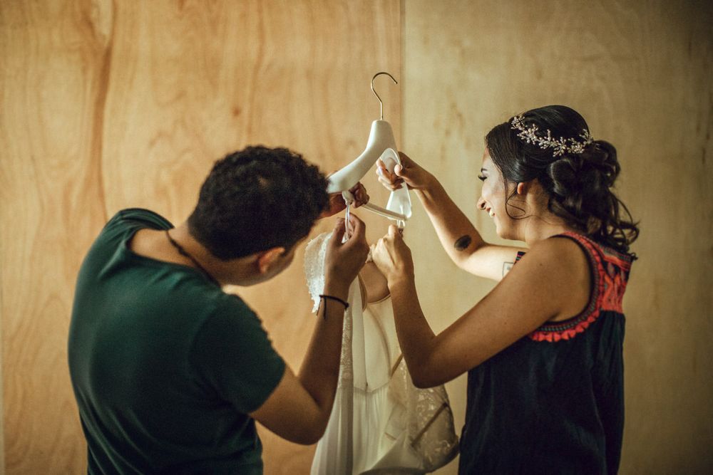 Two people carefully handling a white garment against a wooden wall backdrop.