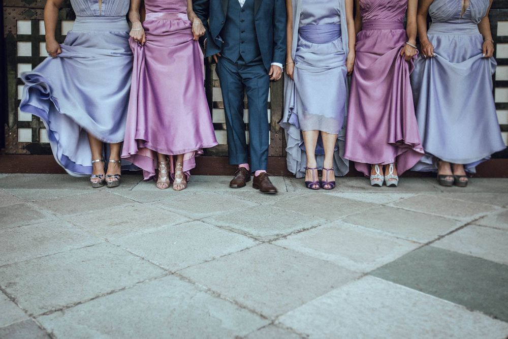 Wedding party members lined up showing elegant dresses in purple, blue and grey with formal shoes.
