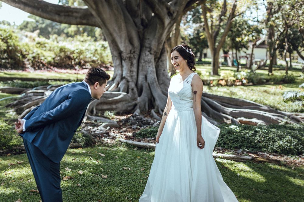 Sweet moment between couple in wedding attire by large garden tree.