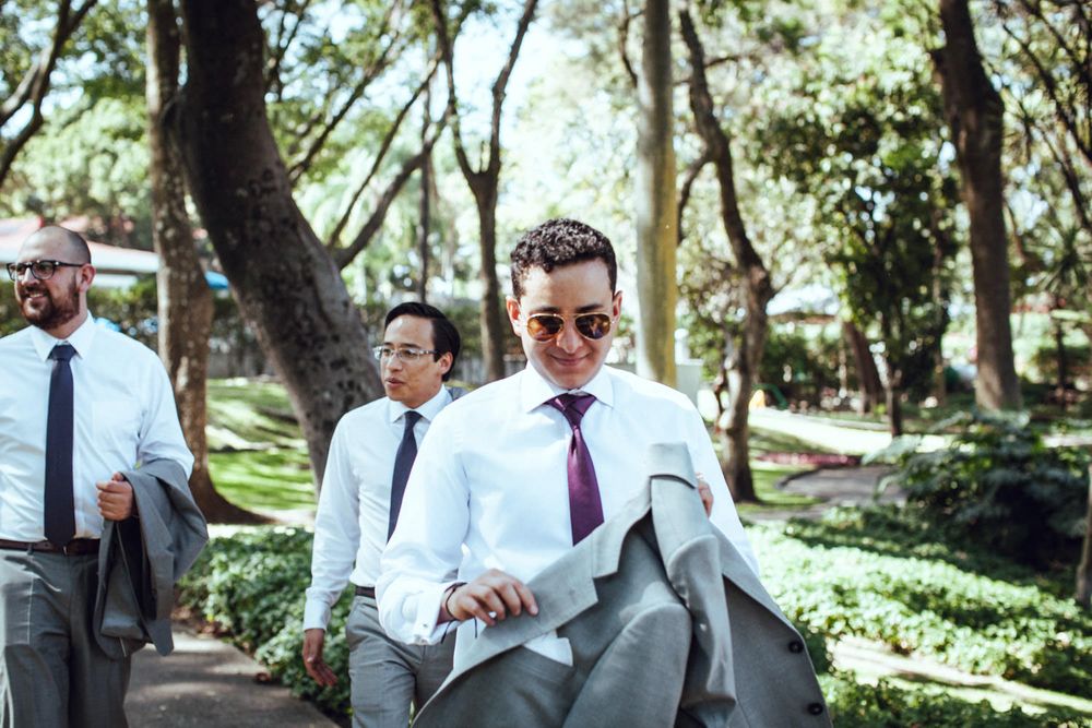 Wedding party members in formal attire walking through a sunny garden pathway.