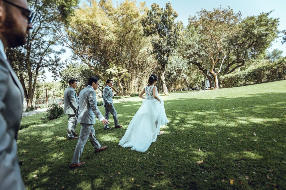Wedding party walking across a sunlit lawn with flowing white dress in motion.