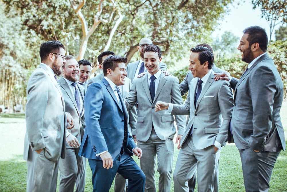 Groomsmen in grey suits and navy jackets gather outdoors for candid group photos.