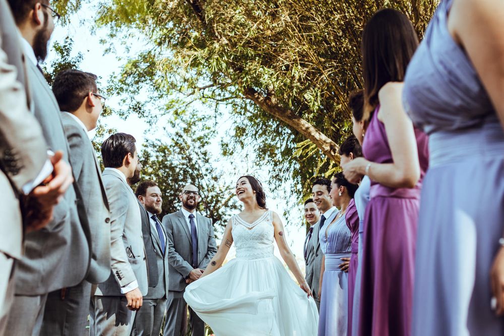 Candid outdoor wedding party photo with bridesmaids in purple and groomsmen in grey.