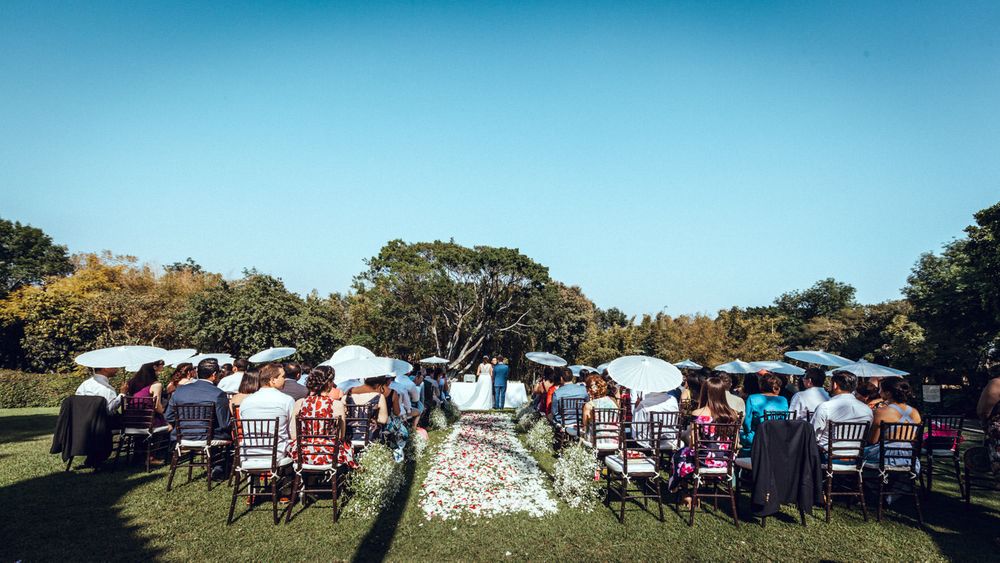 Panoramic view of outdoor wedding ceremony setup with guests seated under blue sky.