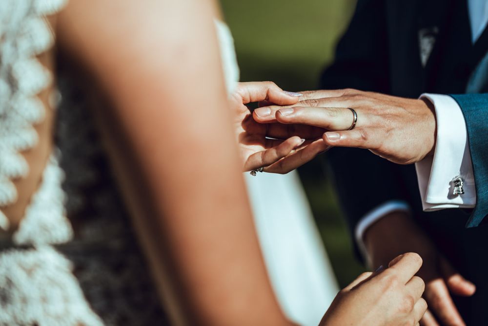 Close-up details of wedding ring exchange during outdoor ceremony.