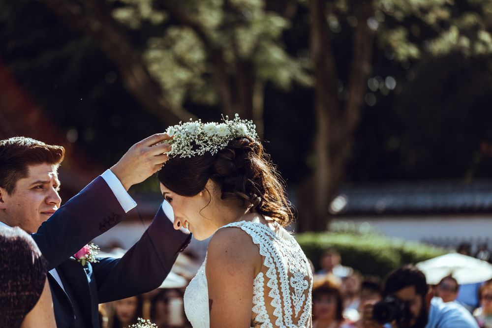 A couple exchanges flower leis during an outdoor wedding ceremony with guests looking on.