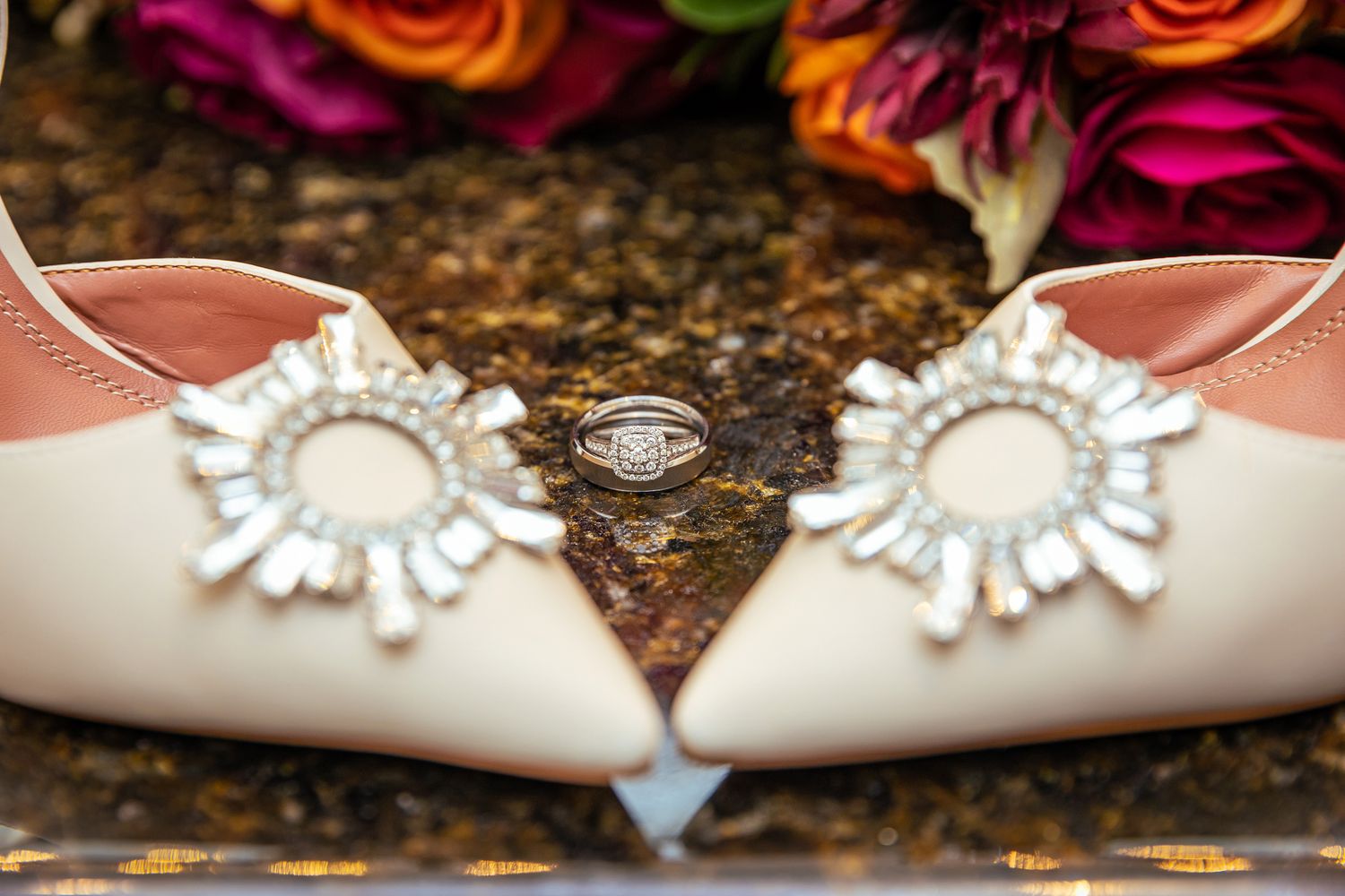 Elegant bridal shoes with ornate embellishments next to a wedding ring.