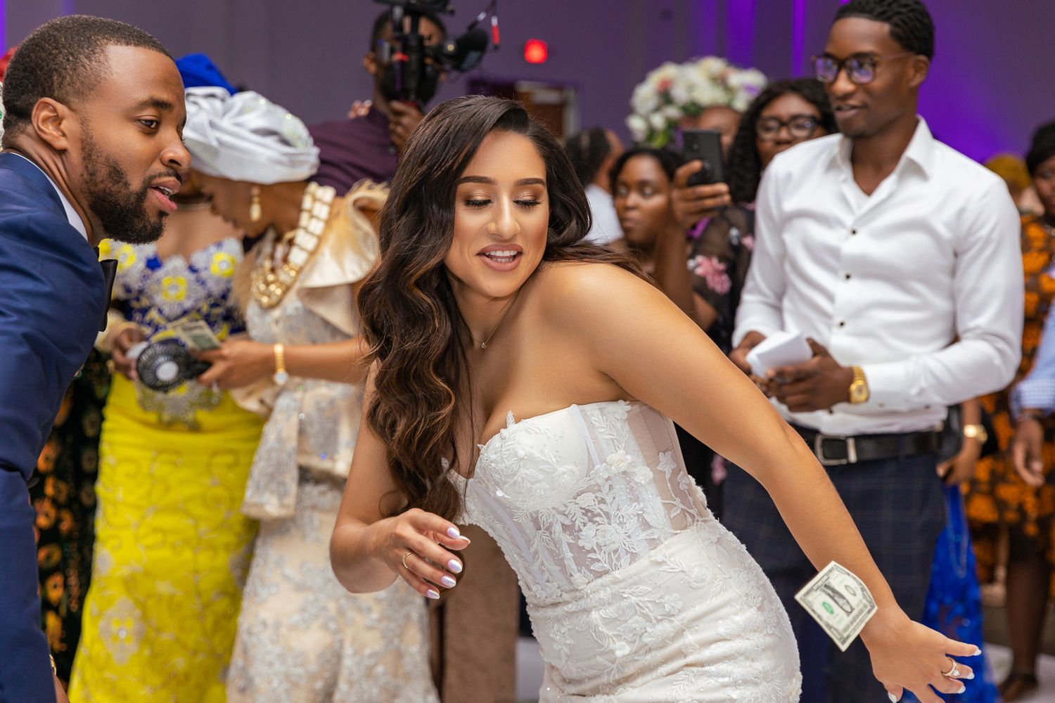 Bride in white dress dancing at reception with guests in background.