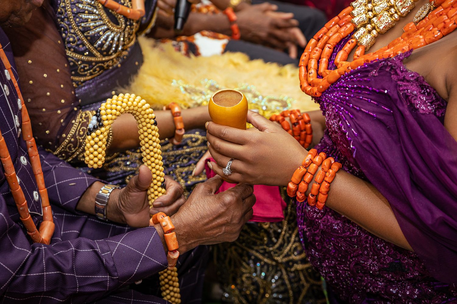 Close-up of hands holding colorful beads and a drink at a festive gathering.