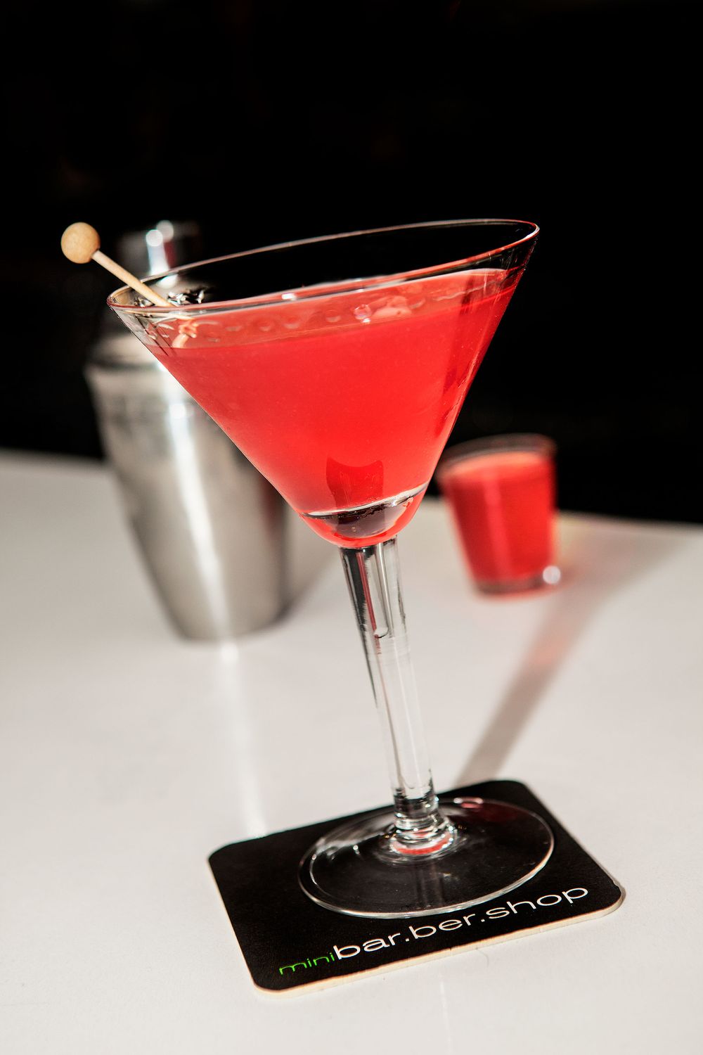 Red martini cocktail in stemmed glass with garnish on branded coaster.