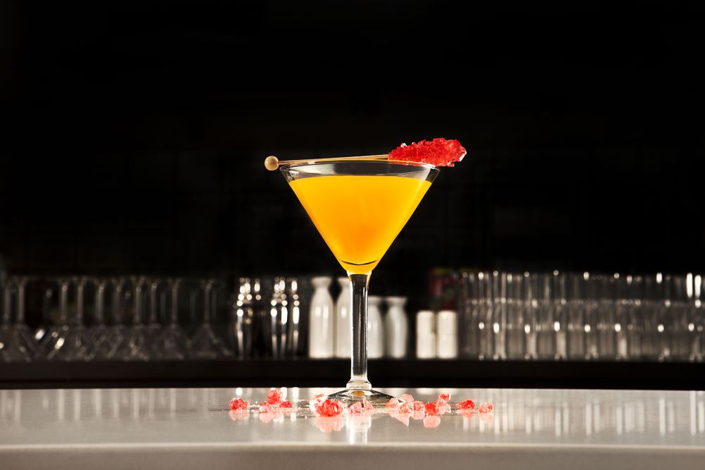 Yellow martini cocktail with cherry garnish against dark bar background.
