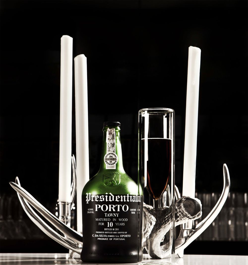 Artistic composition with Porto wine bottle and candle holders on black background.