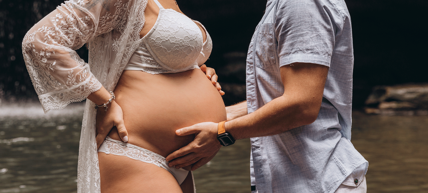 Intimate maternity photo showing hands cradling a pregnant belly in natural lighting.