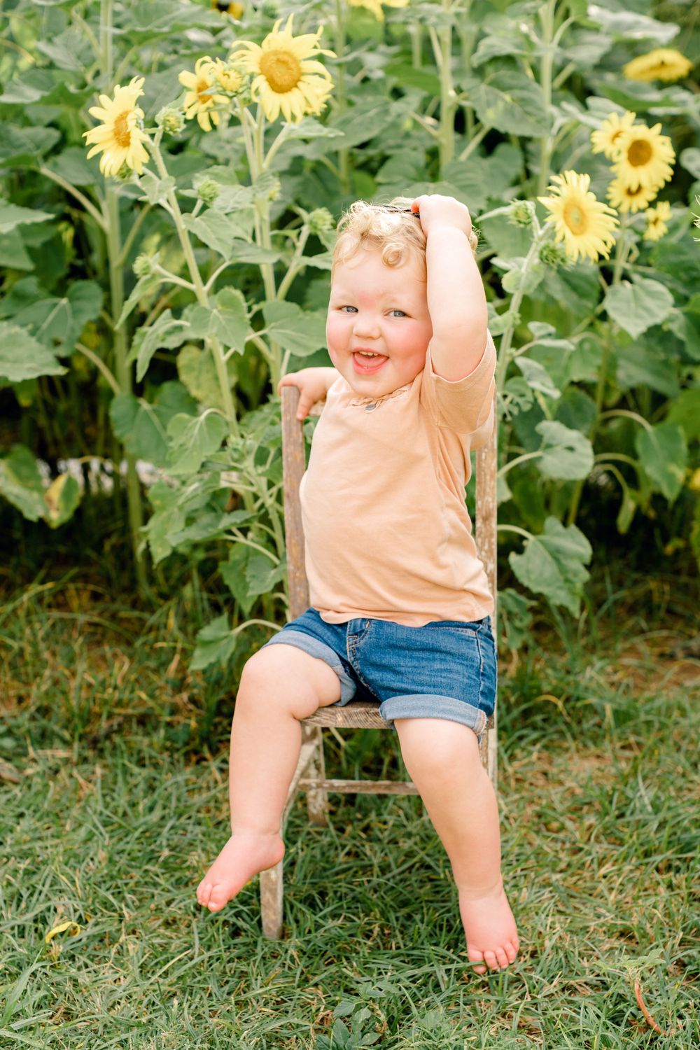 Happy toddler plays on wooden stool in front of blooming sunflower garden.