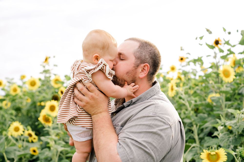 Joyful moment shared between parent and baby in sunflower field.