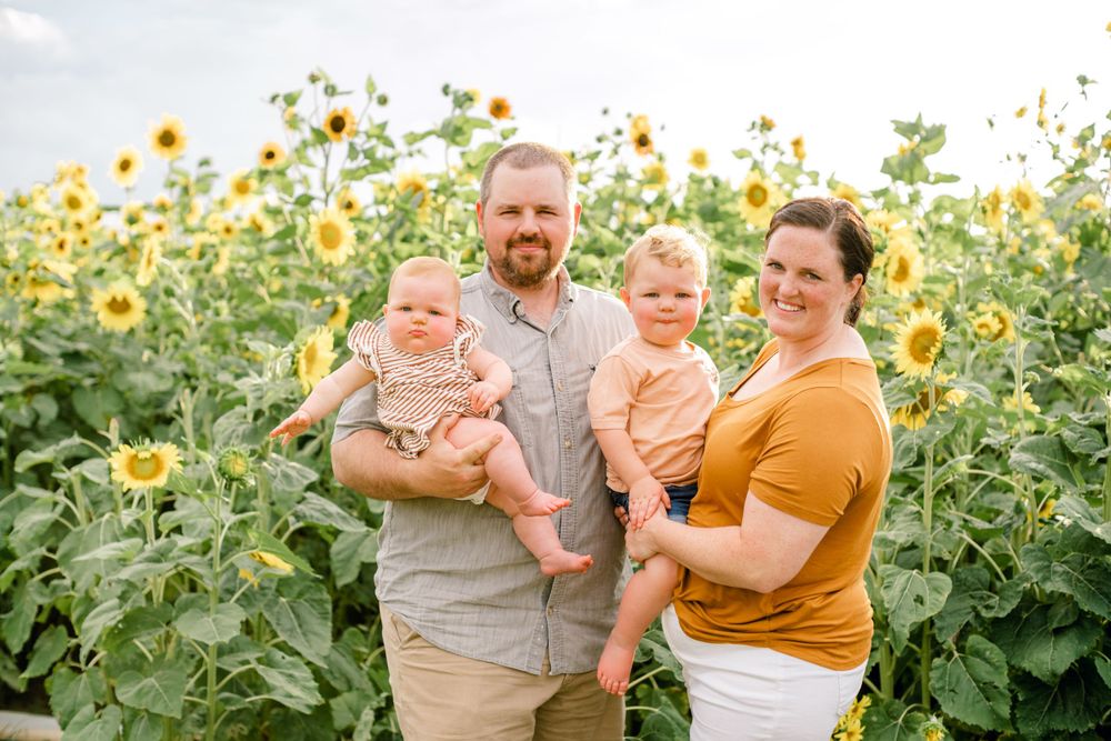 Family poses together for portrait in beautiful sunflower field during sunset.