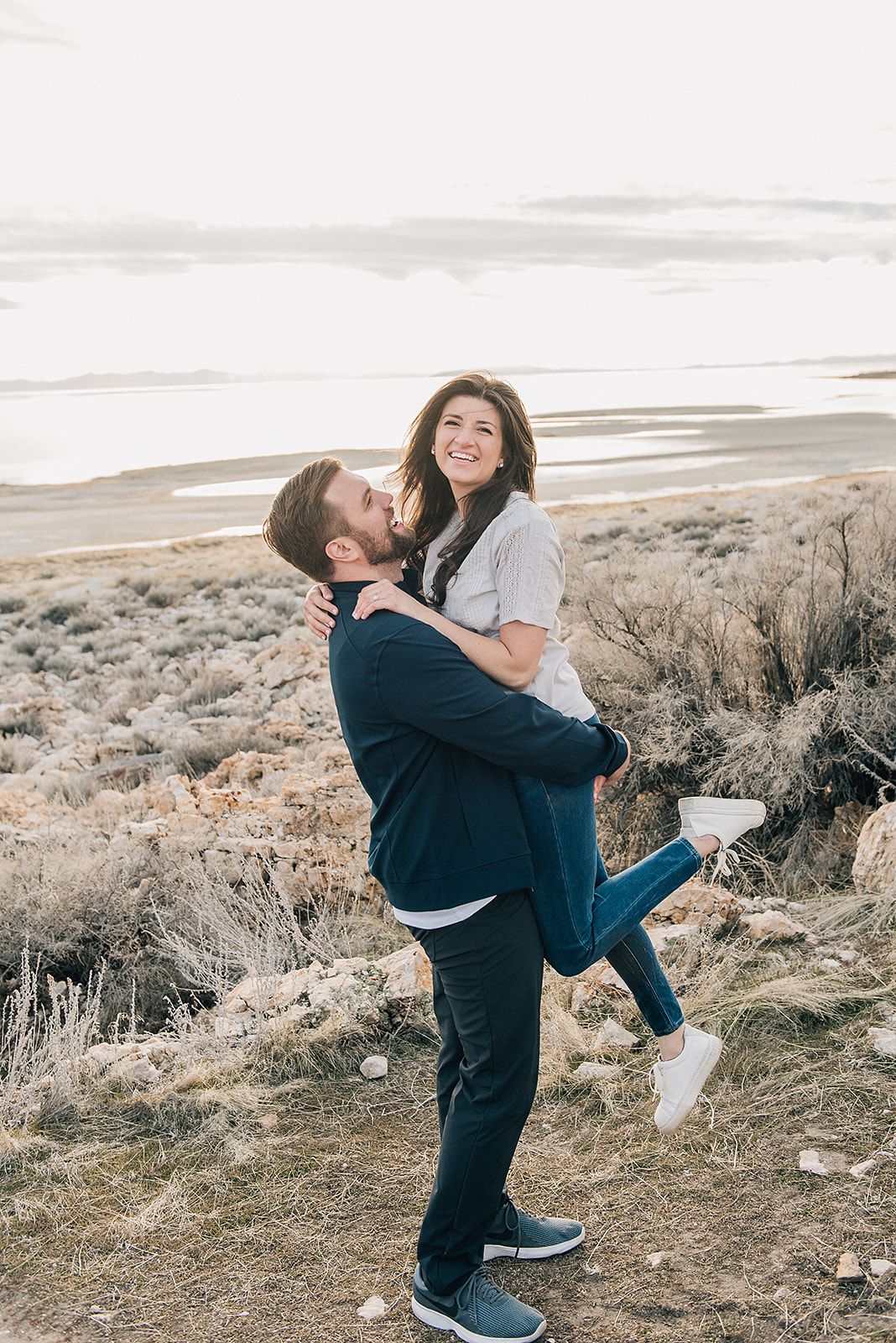 Playful couple embracing on hilltop against scenic desert landscape.