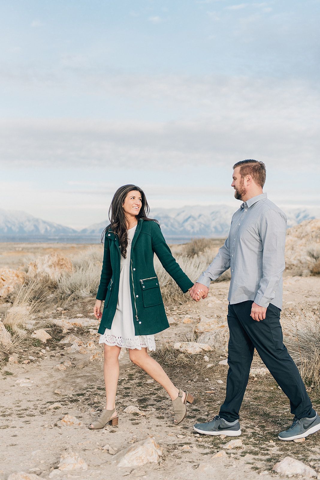 Couple walking hand in hand in desert landscape with mountains in background.