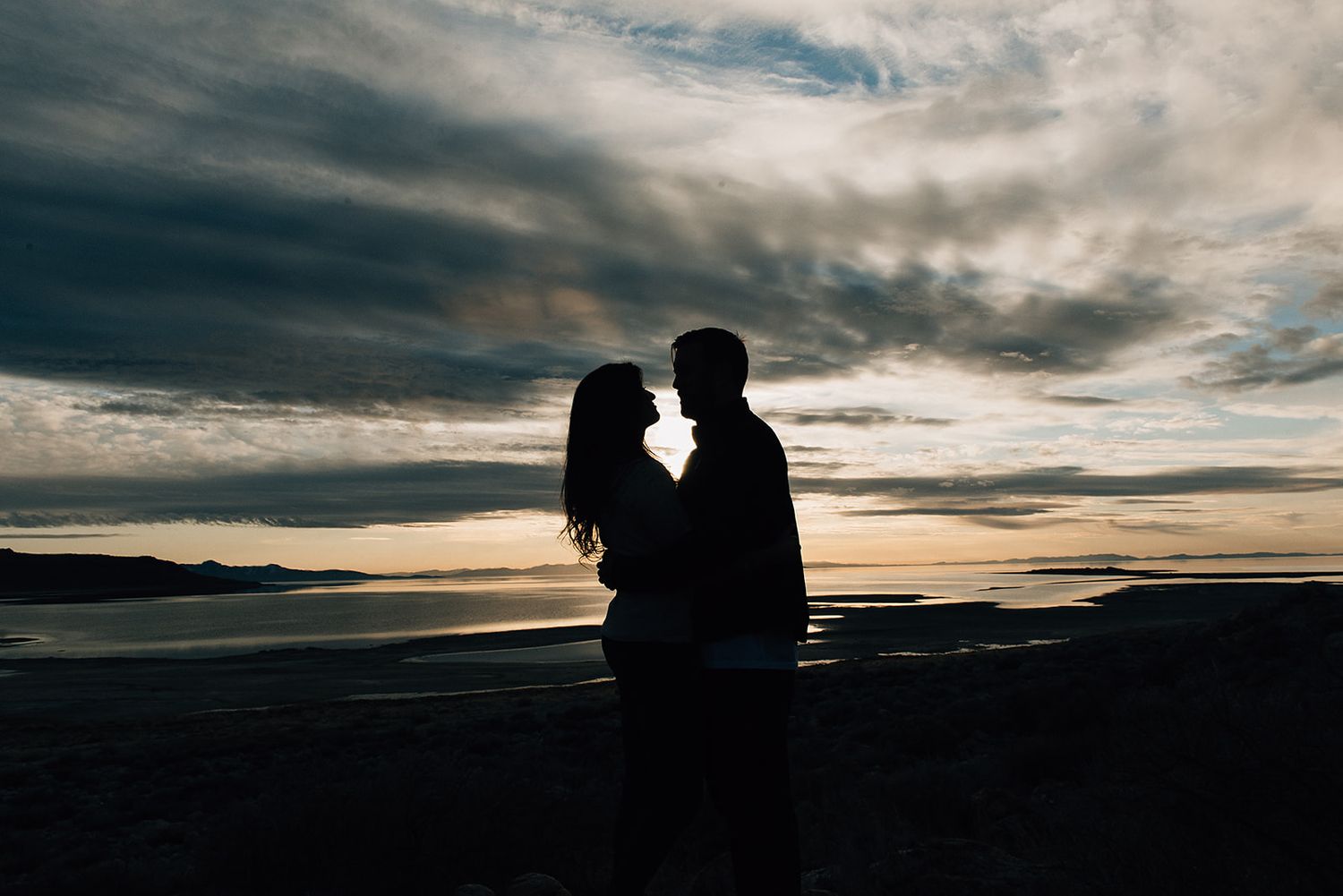 Silhouette of couple against dramatic sunset sky at beach.