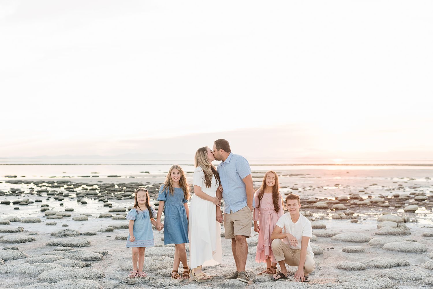Family portrait at sunset on salt flats wearing coordinated blue and white outfits.