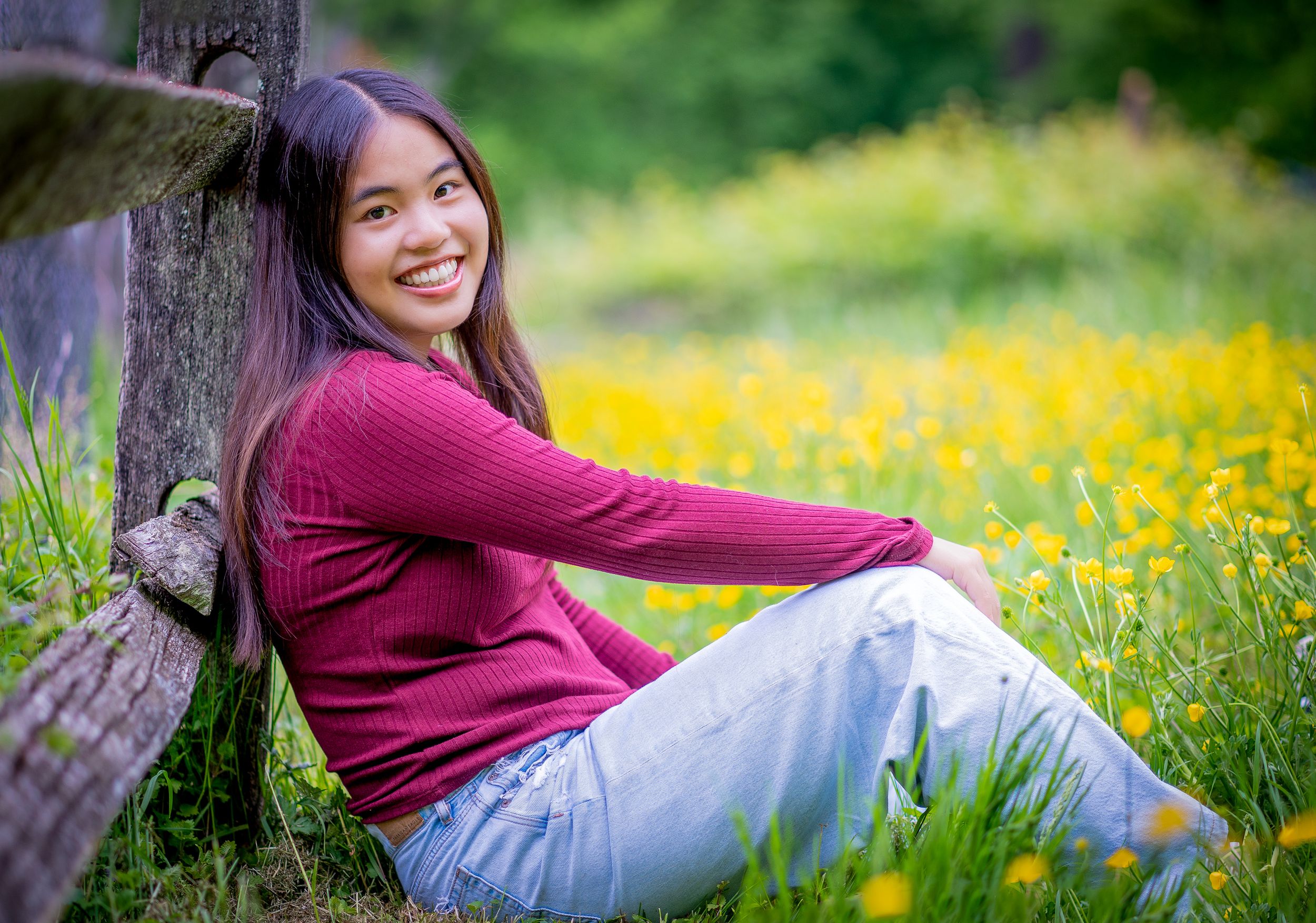 A high school senior leans against a fence post in a field of buttercups in Washington DC.