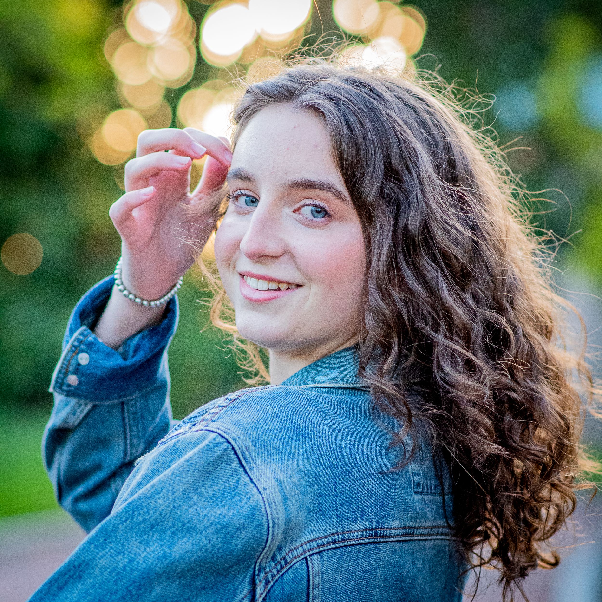 A high school senior brushes the hair out of her eyes and she looks over her shoulder at her senior photographer.