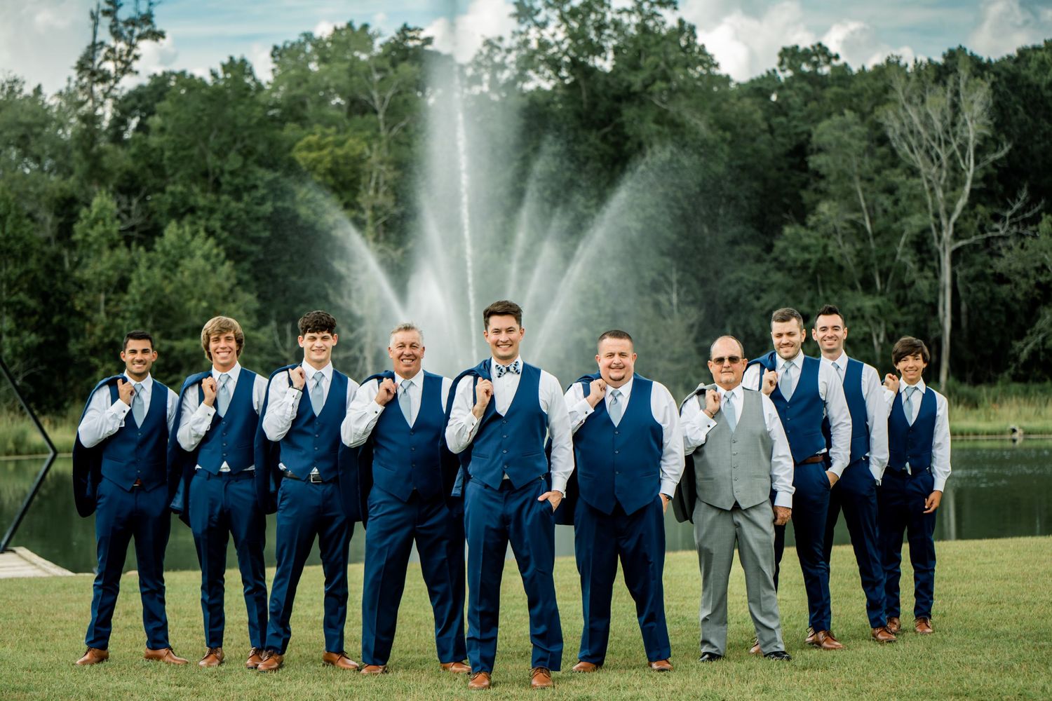 Groomsmen in navy suits pose together outdoors for wedding photos.