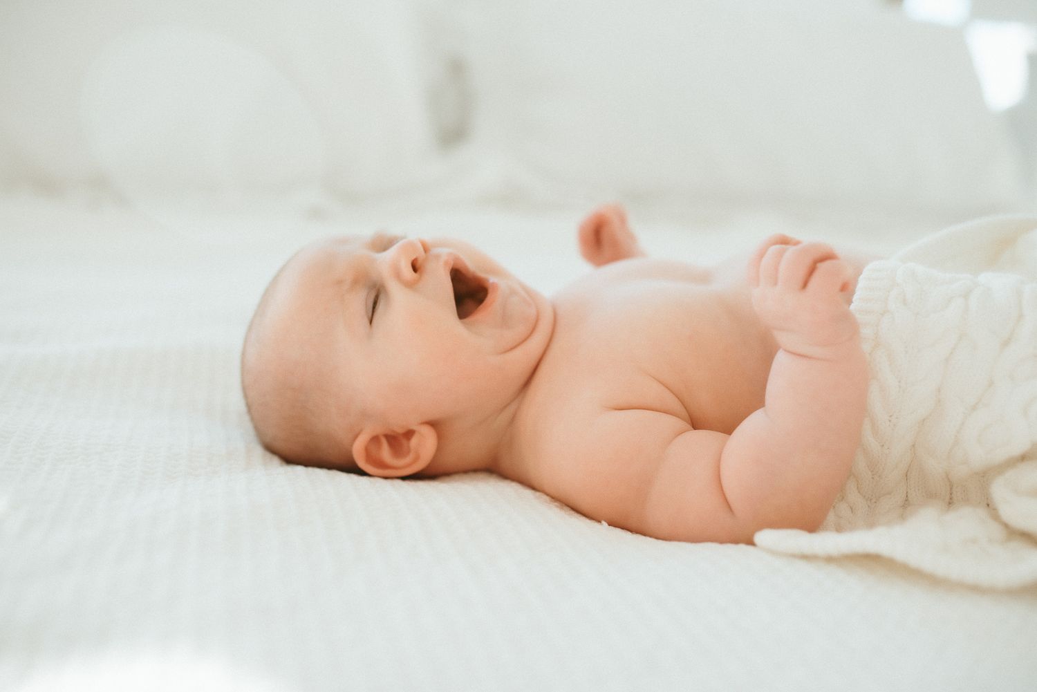 A peaceful sleeping baby lying on white bedding with arms spread wide.