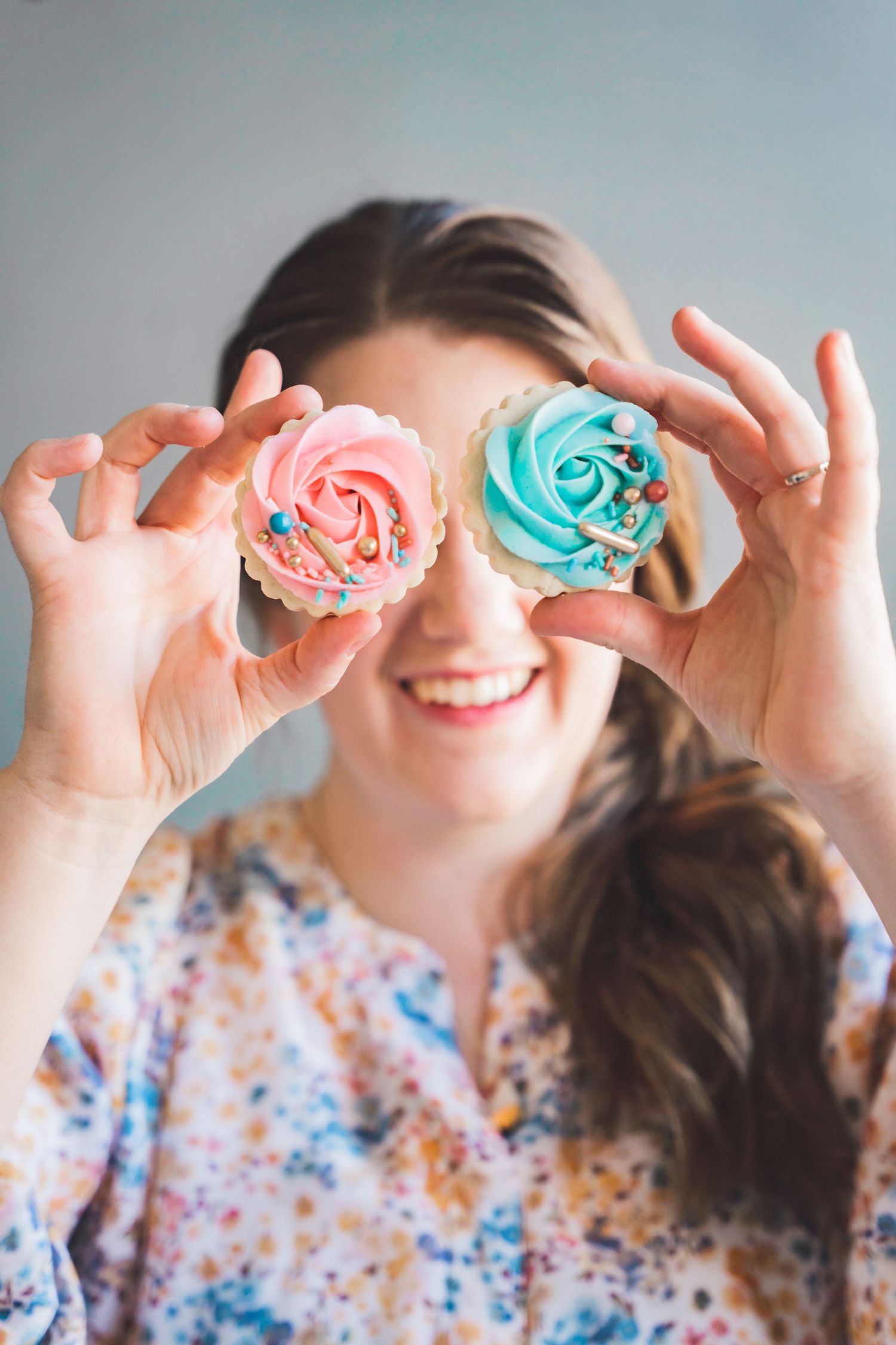 Playful photo of colorful pink and blue frosted cupcakes held up to eyes.
