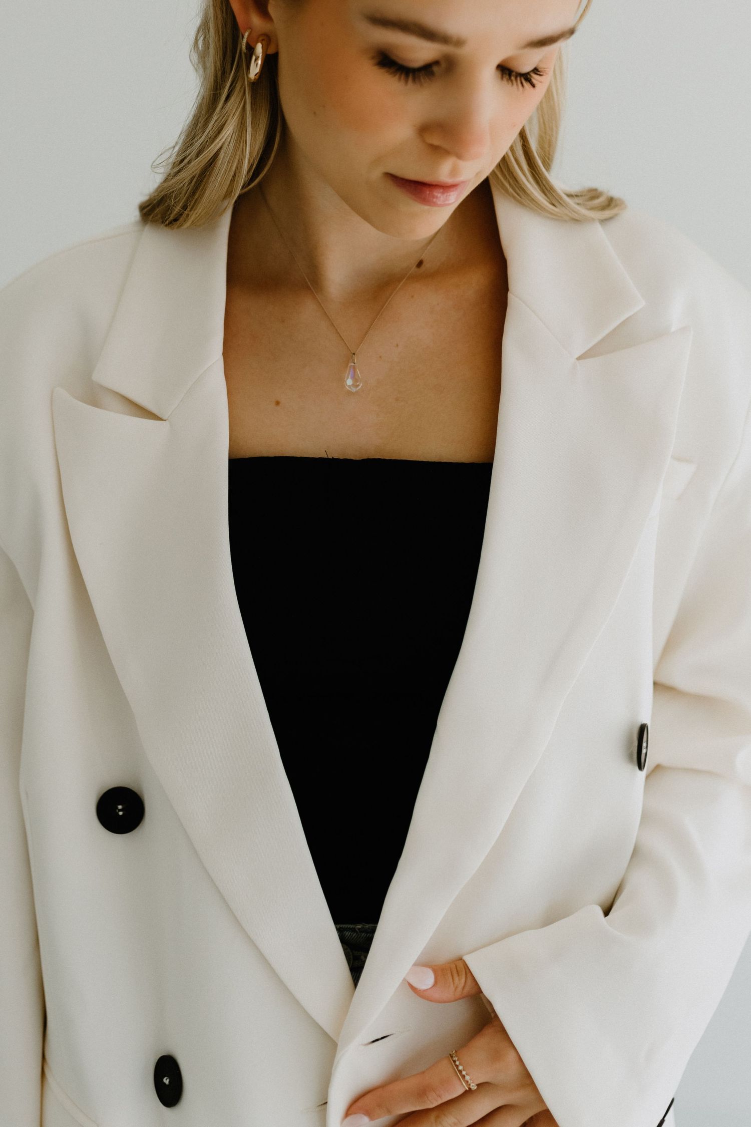 A crisp white blazer styled with a black top and delicate necklace in a minimalist fashion portrait.