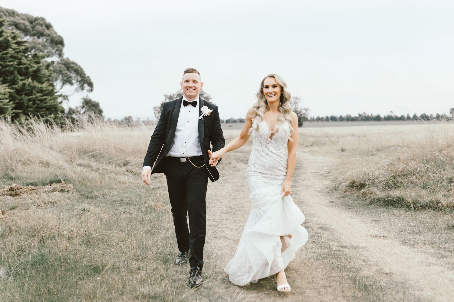 A wedding couple walking along a countryside path in formal attire.