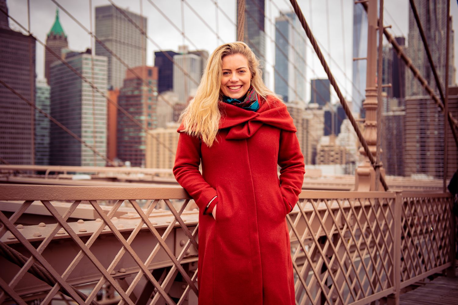 Model in a Burnt Orange Coat on the Brooklyn Bridge with the New York City Skyline in the Background.