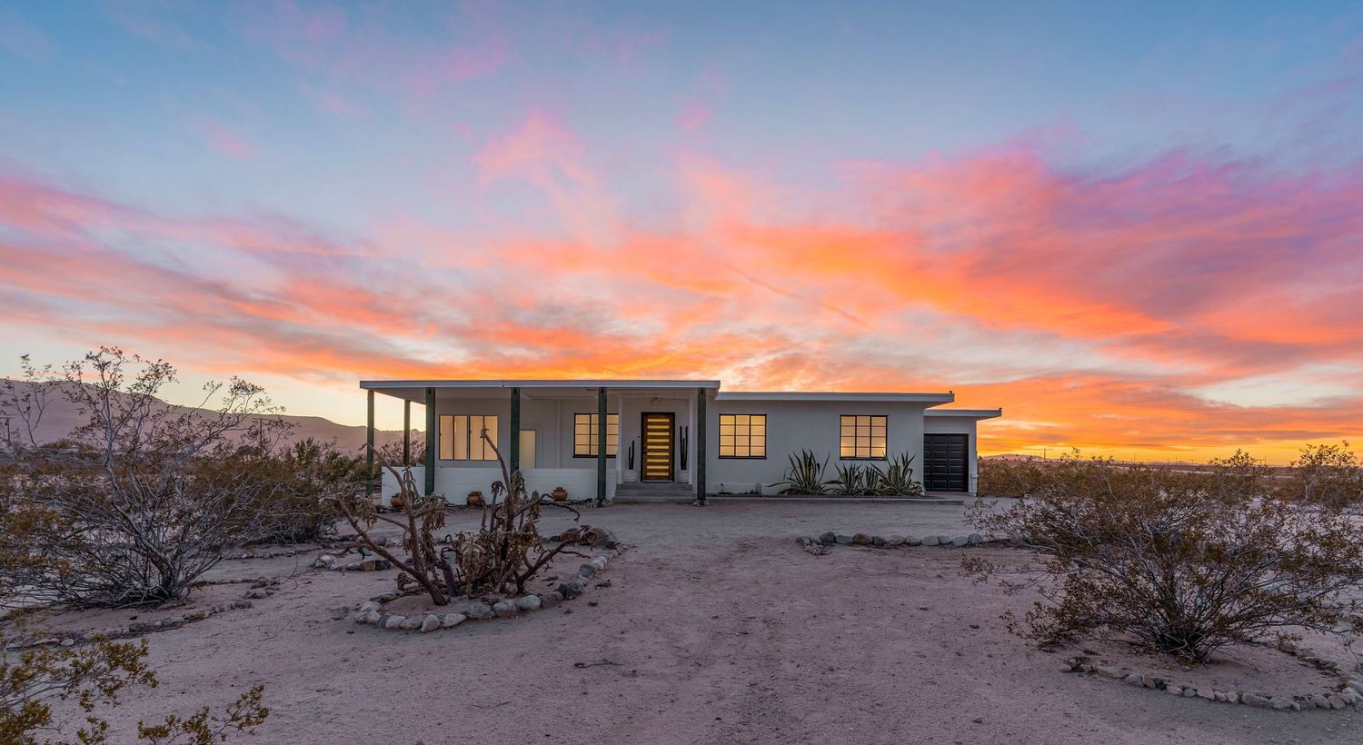 Panoramic desert sunset with vibrant pink and orange clouds stretching across the horizon over mountain silhouettes.