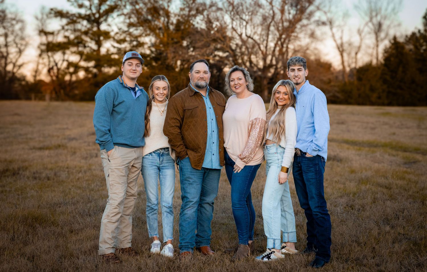 A group of six people stand together outdoors in casual clothing at sunset in an open field.