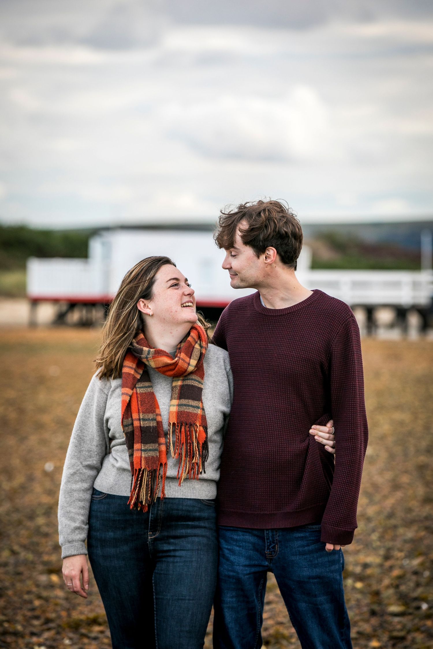 A couple shares a playful moment while walking through a field on an overcast day.