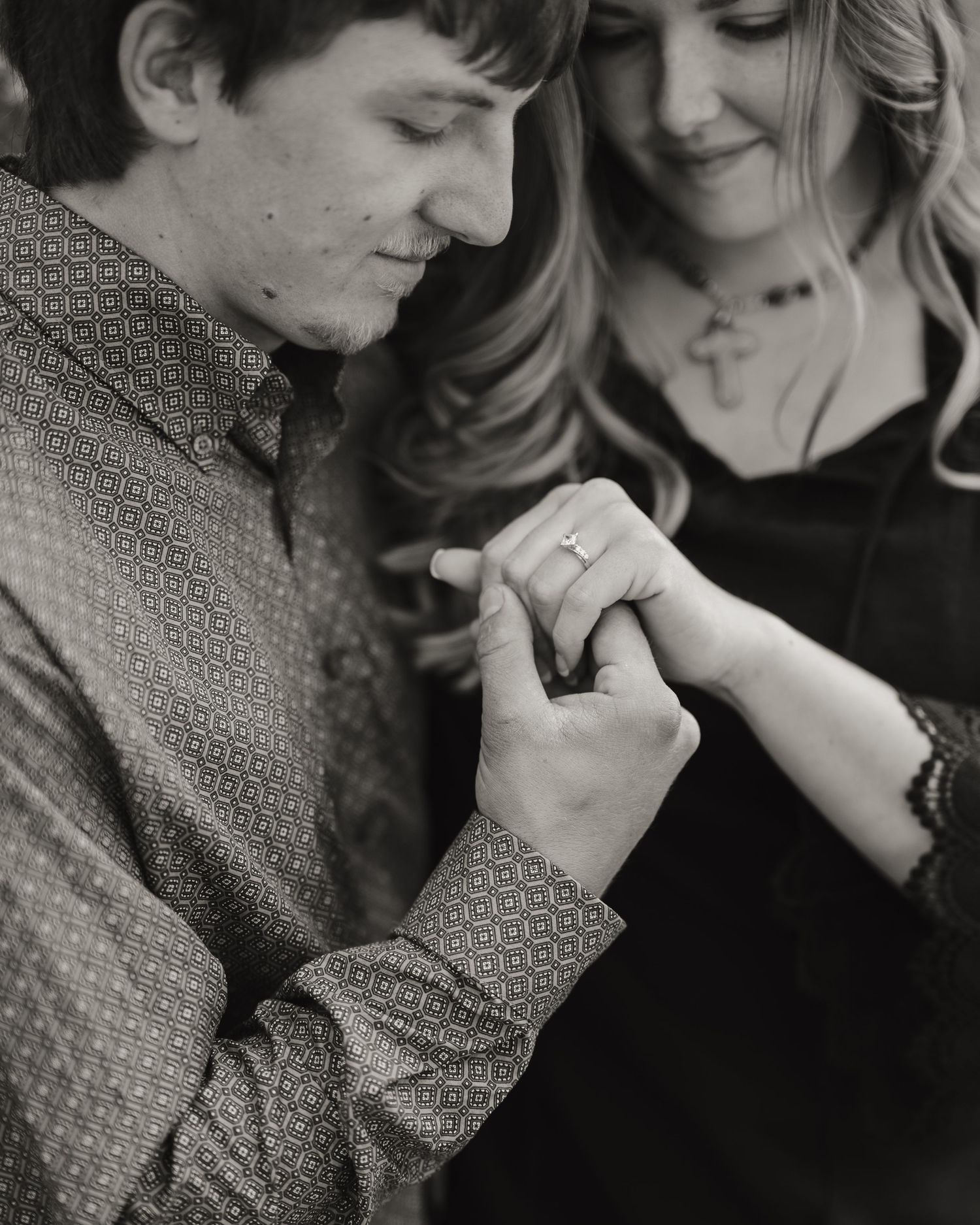 A black and white engagement photo focusing on hands and rings in an intimate moment.