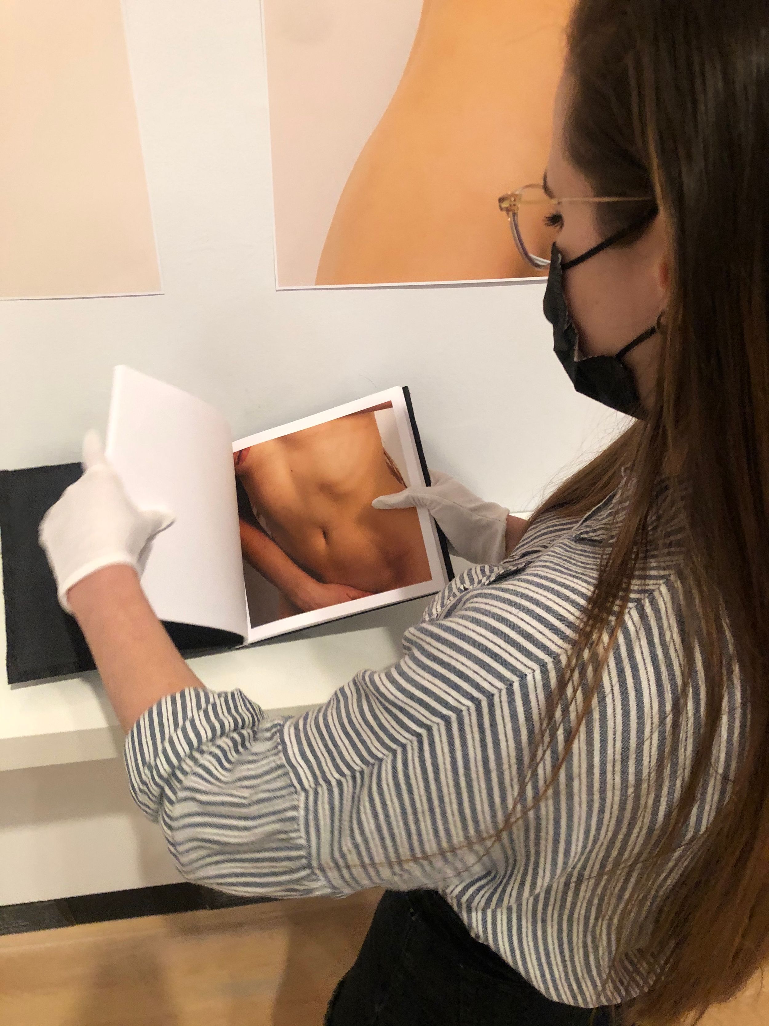 Woman in gloves and mask carefully examining a photography book at an art gallery exhibition.