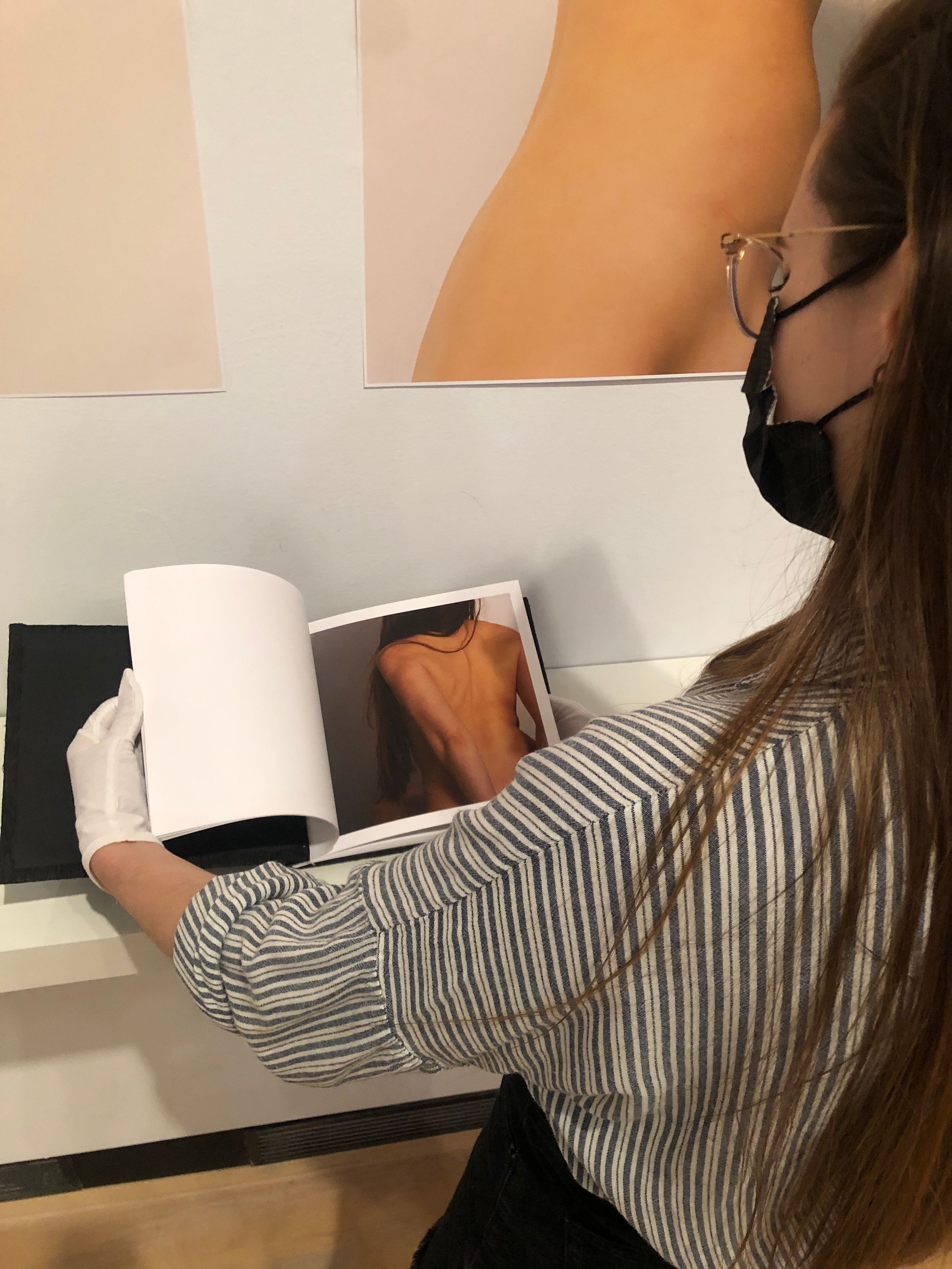 Woman wearing white gloves and mask flipping through an art photography book at a gallery display.