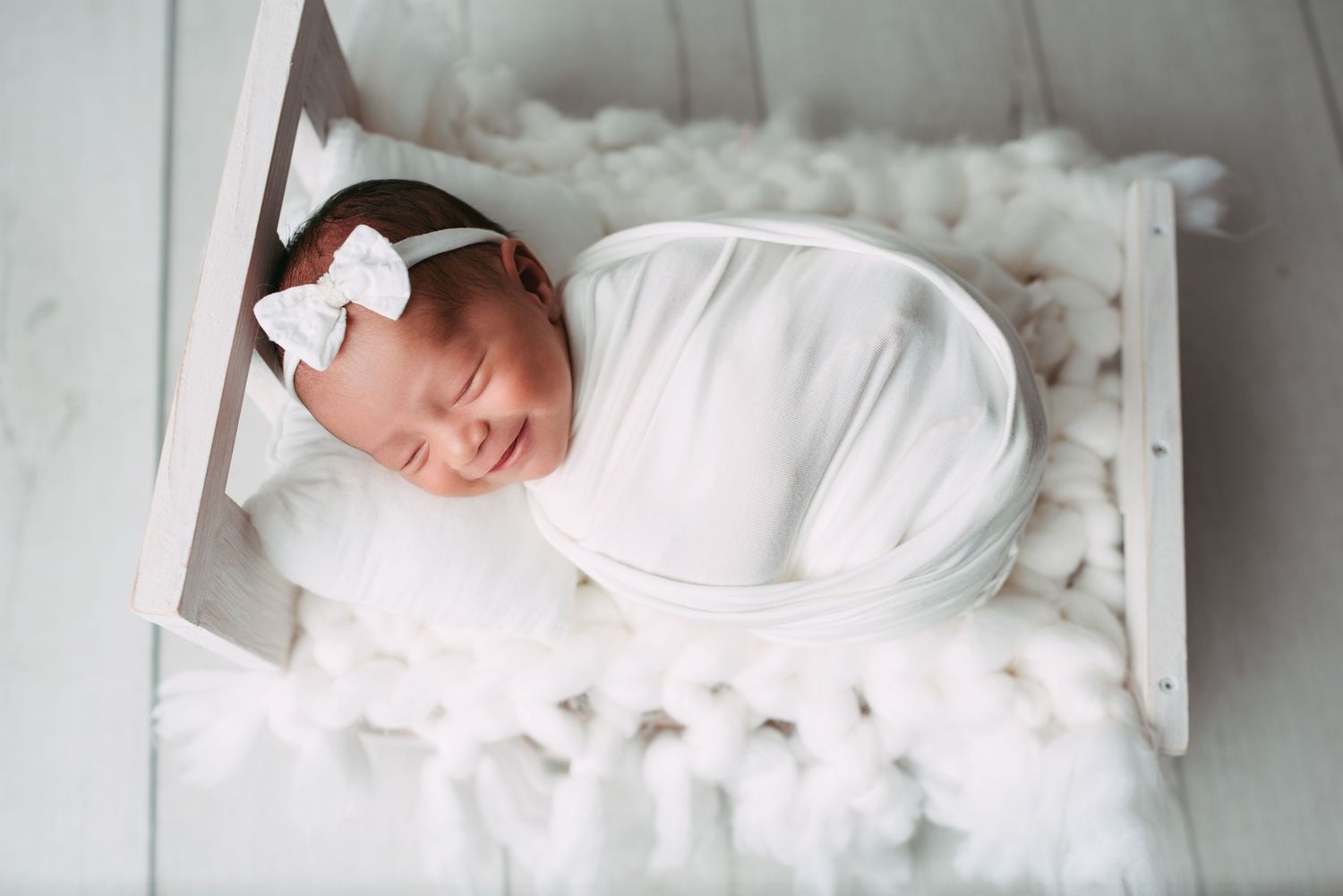 newborn baby smiling while sleeping in a little white  bed during a newborn  photoshoot