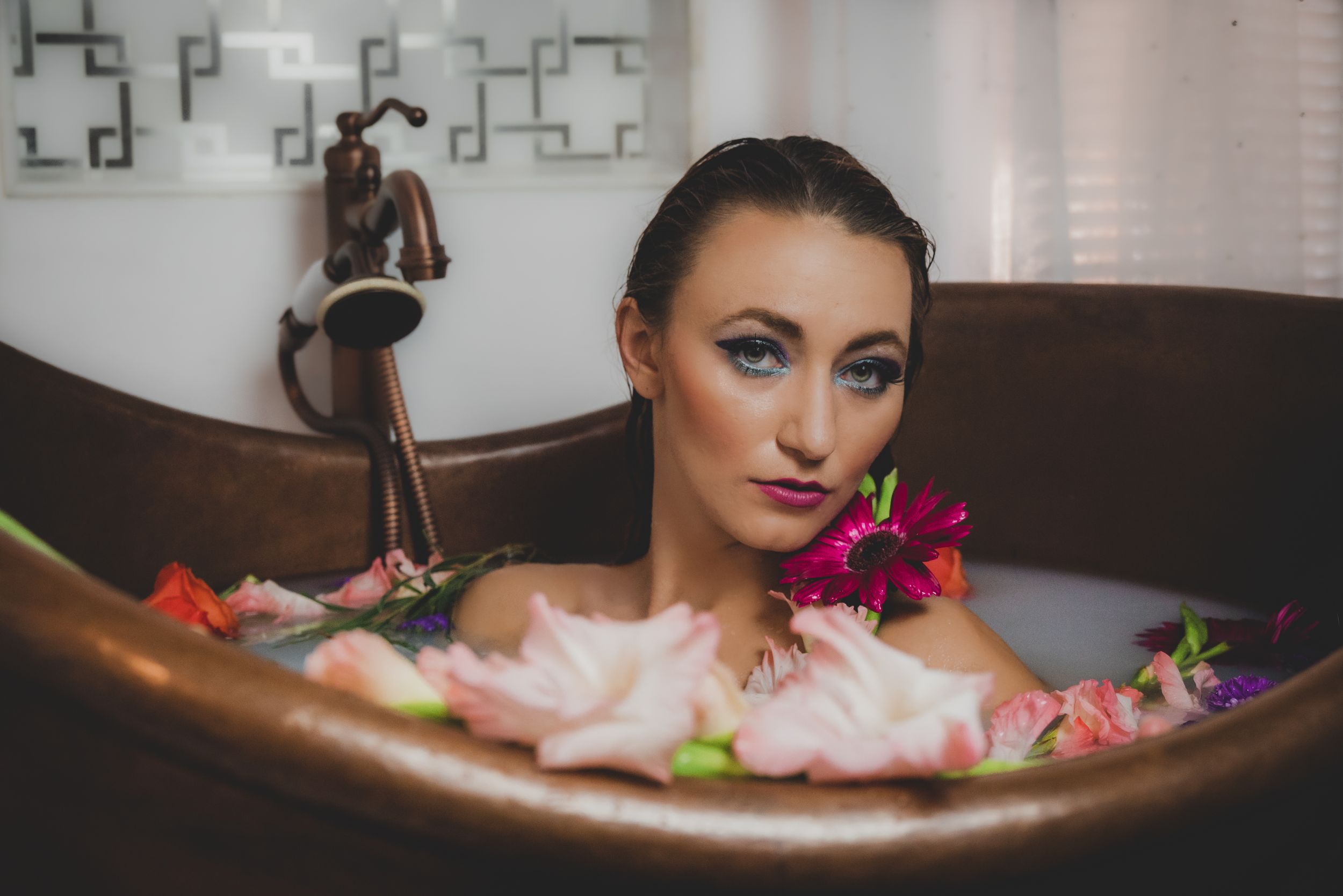 Elegant woman relaxing in copper clawfoot bathtub surrounded by colorful fresh flowers in a milk bath.