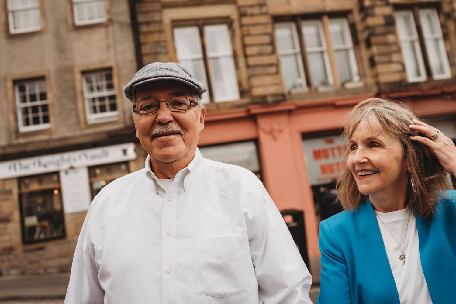 A cheerful older couple shares a moment on an Edinburgh street with historic buildings behind them.