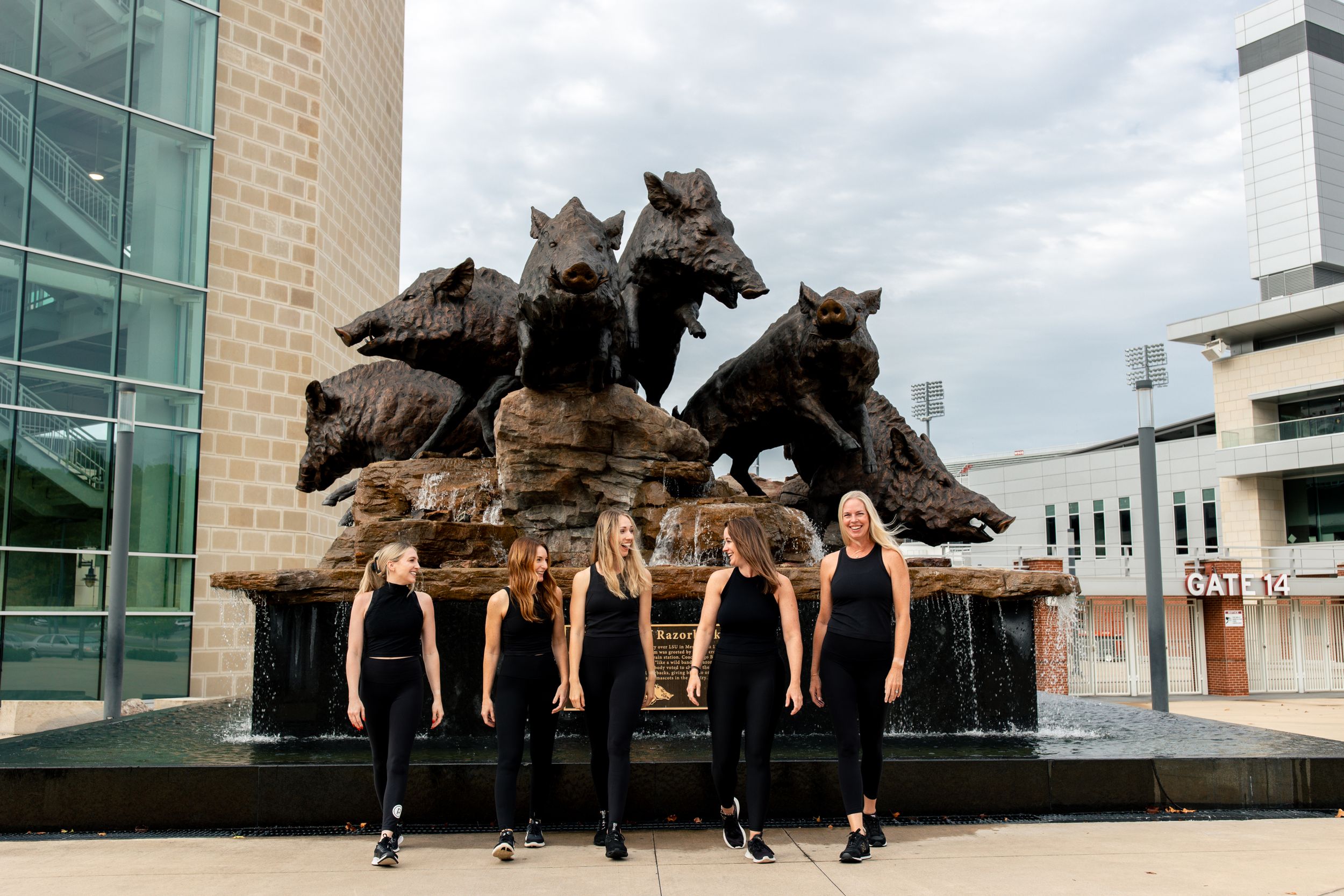 Group in black athletic wear poses in front of large bronze horse statue sculpture at modern building entrance.