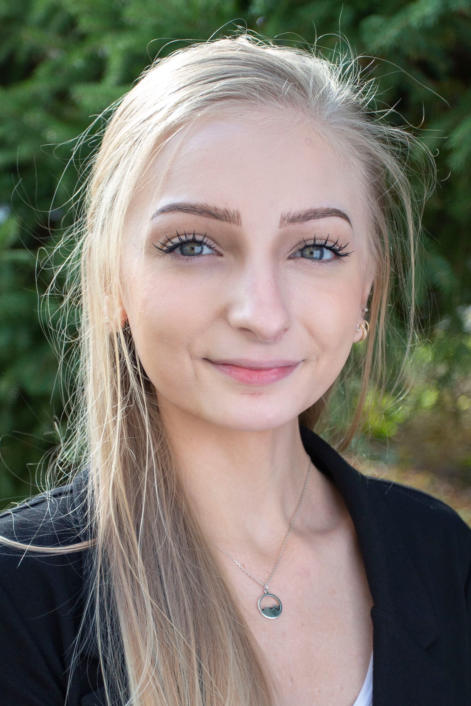 Close-up portrait outdoors with natural greenery background and soft lighting.