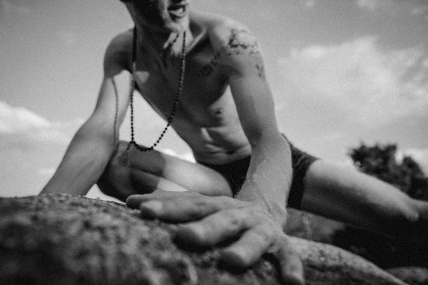 Black and white artistic photograph showing tattooed torso on rocks outdoors.