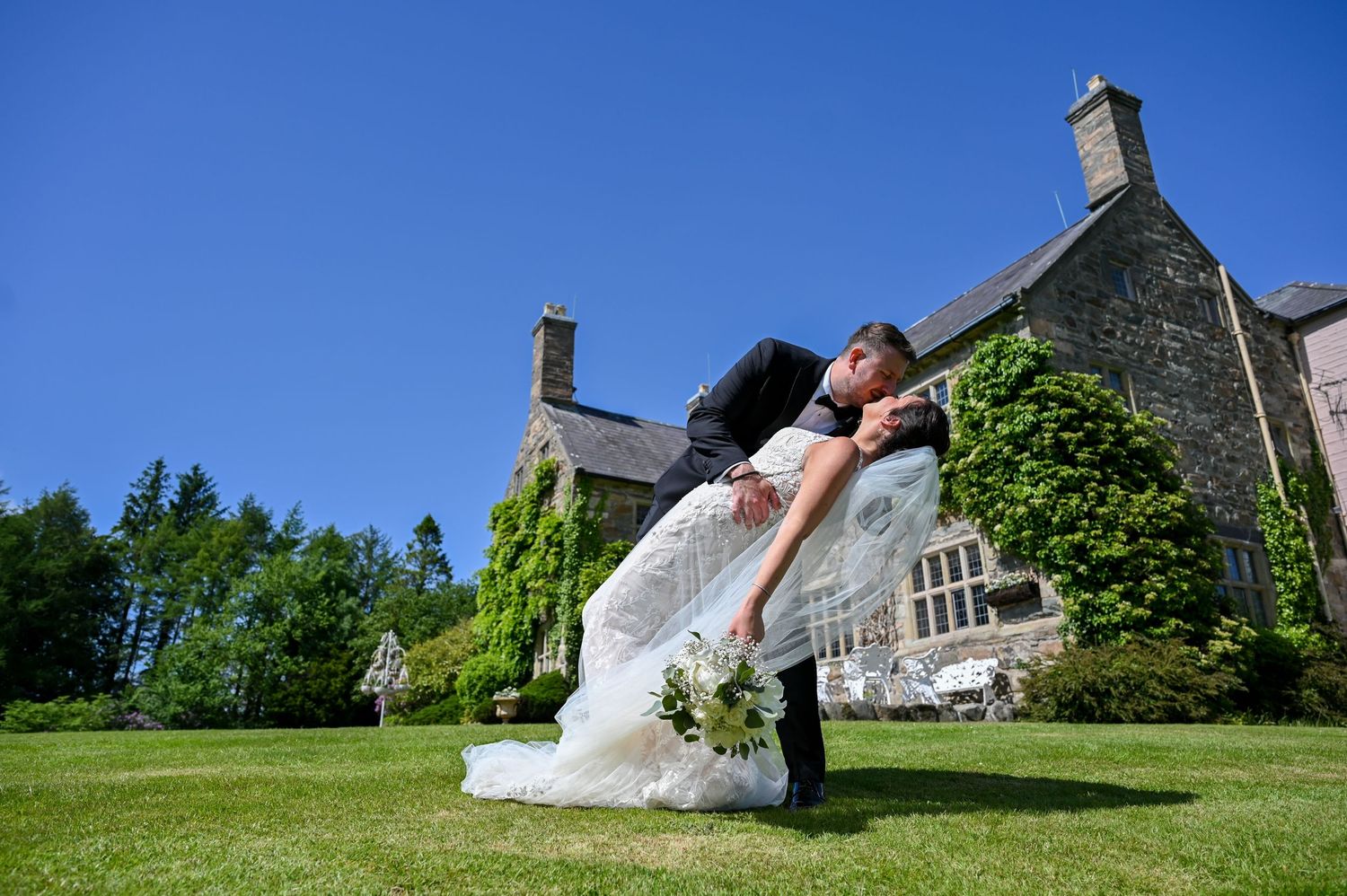 A dramatic dip pose with the bride's dress flowing against a stone building and blue sky.