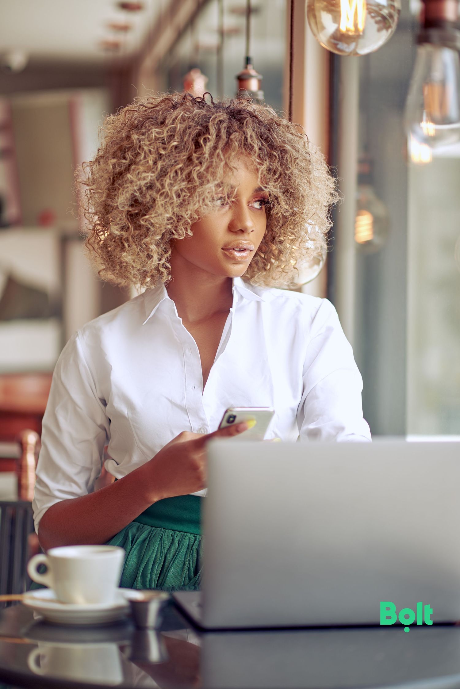 Person with curly blonde hair works on laptop in cafe setting.