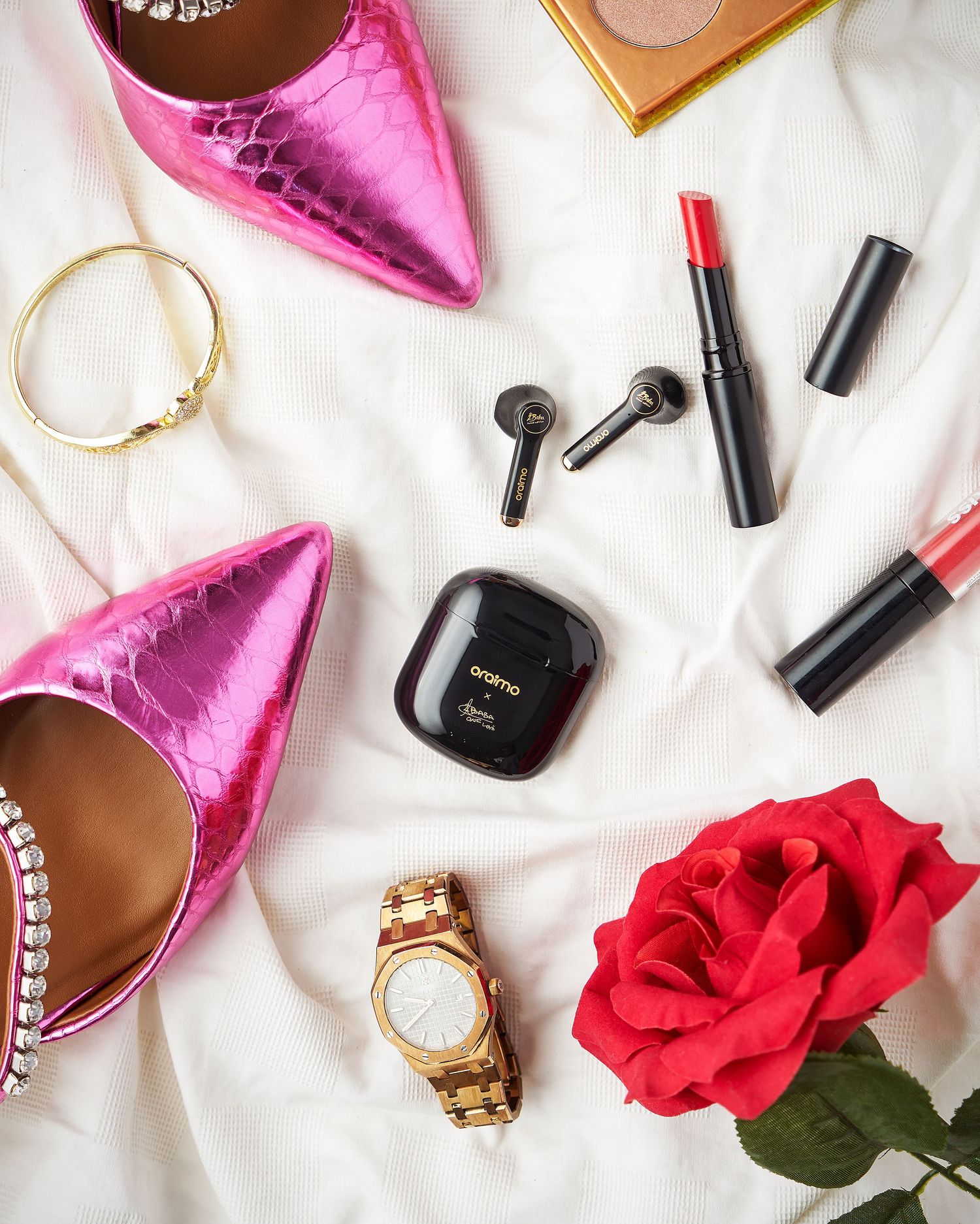 Pink metallic high heels, red rose, makeup items and jewelry arranged on white background.